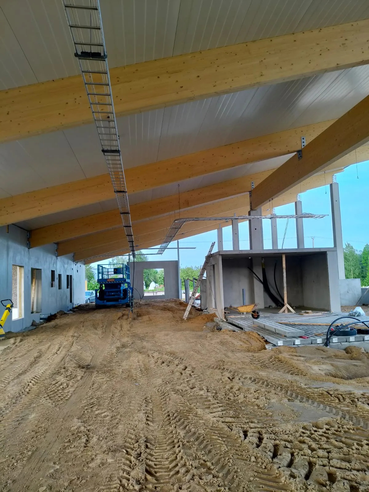 Rakennusprojekti sisätiloissa, jossa on puurakenteinen katto ja maapohja, rakennustelineitä ja työkaluja.