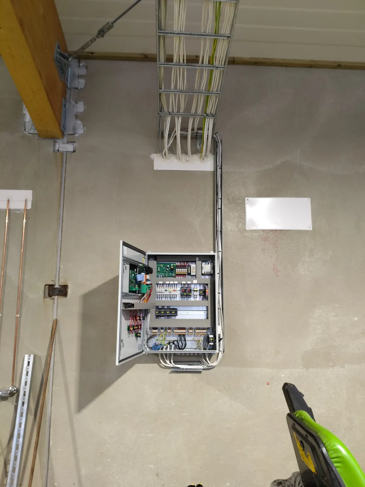 Avoin sähkökaappi, jossa on johdot ja piirikortteja betoni- ja puuankkuroinnin ympäröimällä tehdas- tai varastotilan seinällä.